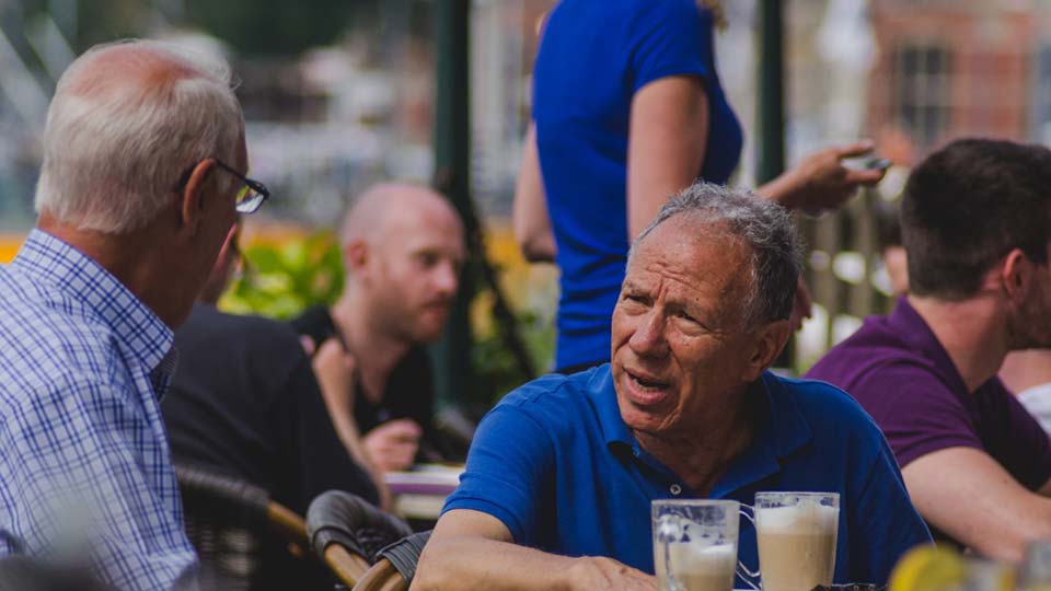 Two men have a conversation over a table at an outdoor café. Photo: Unsplash