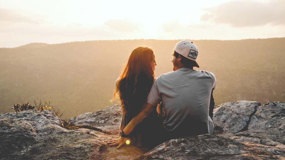 A young couple sitting on a hilltop watches the sunrise. Photo: Unsplash
